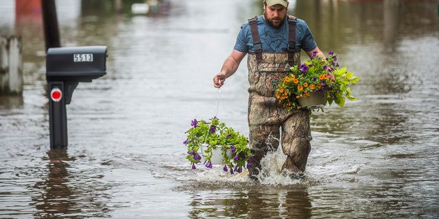 Tyler Marciniak, of Grand Rapids, carries hanging plants through floodwaters as he helps his father, Tom Marciniak, assess the damage to his home on Red Oak Drive on Wixom Lake, Tuesday, May 19, 2020, in Beaverton, Mich.