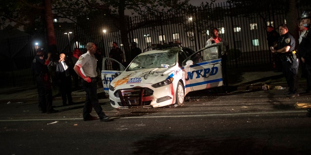 Policemen surround a NYPD vehicle after it was vandalized by protestors over the death of George Floyd, a black man who was in police custody in Minneapolis, on Saturday, May 30, 2020, in the Brooklyn borough of New York. Floyd died after being restrained by Minneapolis police officers on Memorial Day.
