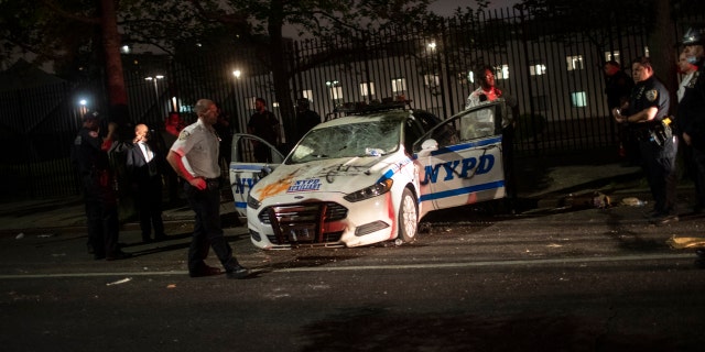 Policemen surround a NYPD vehicle after it was vandalized by protestors over the death of George Floyd, a black man who was in police custody in Minneapolis, on Saturday, May 30, 2020, in the Brooklyn borough of New York. Floyd died after being restrained by Minneapolis police officers on Memorial Day.