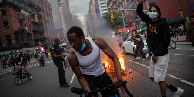 Protesters march down the street as trash burns in the background during a solidarity rally for George Floyd, Saturday, May 30, 2020, in New York.