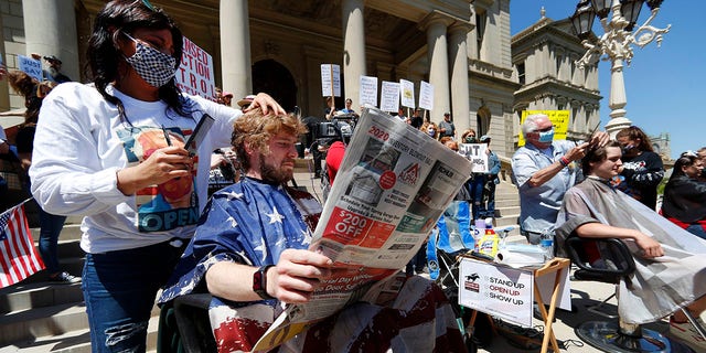 Jody Hebberd, left, gives a free haircut to Reid Scott, as he reads the paper on the steps of the State Capitol as Karl Manke, right, cuts the hair of Parker Shonts during a rally in Lansing, Mich., on Wednesday. (AP Photo/Paul Sancya)
