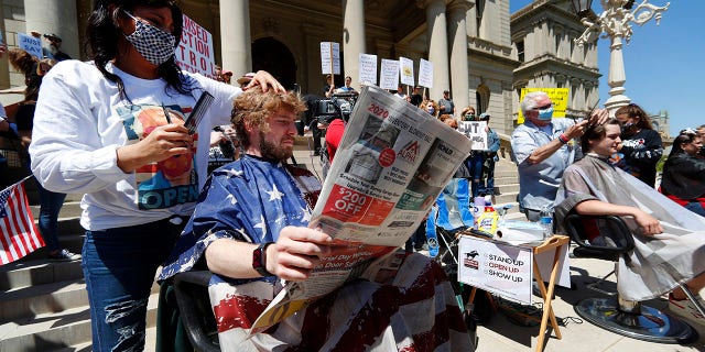 Jody Hebberd, left, gives a free haircut to Reid Scott, as he reads the paper on the steps of the State Capitol as Karl Manke, right, cuts the hair of Parker Shonts during a rally in Lansing, Mich., on Wednesday. (AP Photo/Paul Sancya)