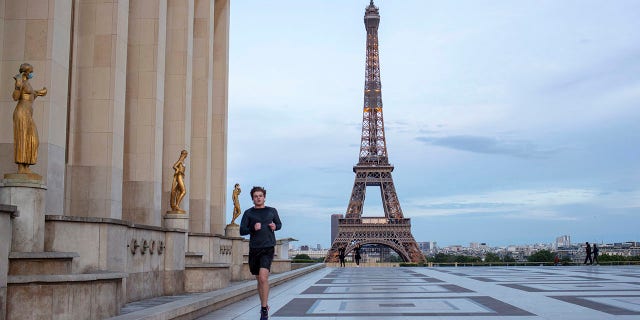 A man runs past some statues wearing face masks along the Trocadero square close to the Eiffel Tower during the coronavirus pandemic on Saturday. (AP Photo/Rafael Yahgobzadeh)