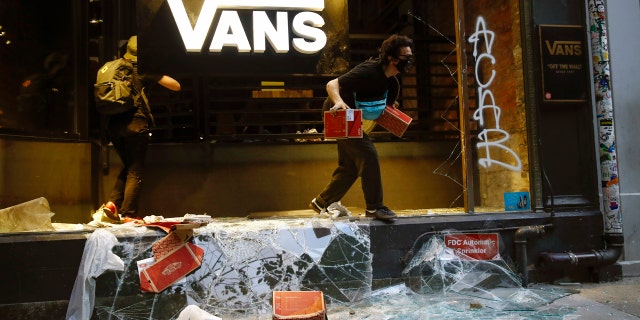 A person jumps from a storefront that had its window broken during the Justice for George Floyd Philadelphia Protest on Saturday, May 30, 2020.