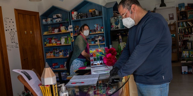 A stationary shop owner attends a customer in La Cabrera, outskirts of Madrid, Spain, Wednesday, May 6, 2020. The country enters the first stage of its 4-phase lockdown rollback helped by the lowest daily reports of coronavirus related deaths from coronavirus in 1.5 months.