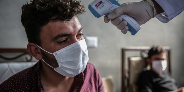 A medic checks the temperature of a man inside a health isolation centre which has been established on the Syrian-Turkish borders in order to place people coming from Turkey to Idlib as a preventive measure against the spread of the coronavirus disease (COVID-19).