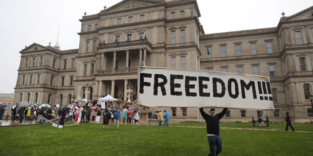 A protester carries a sign during a rally against MichiganÕs coronavirus stay-at-home order at the State Capitol in Lansing, Mich., Thursday, May 14, 2020. (AP Photo/Paul Sancya)