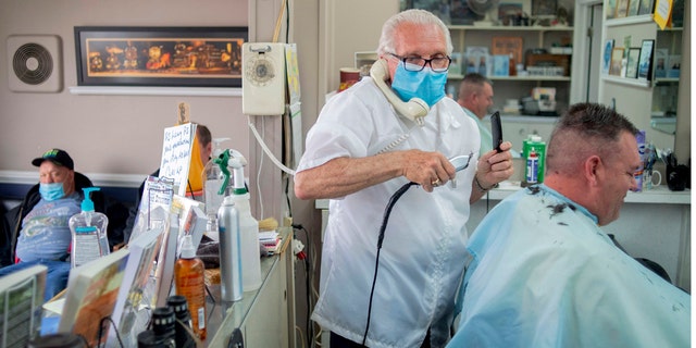 Karl Manke, 77, left, wears a mask while cutting hair, May 5, at Karl Manke's Barber and Beauty Shop in Owosso, Mich. Manke re-opened his doors on Monday in defiance of Gov. Gretchen Whitmer's executive order mandating salons, barbershops and other businesses to stay closed. He has already given nearly 100 haircuts, and fields more calls than that daily, all while continuing to cut hair. (Jake May/The Flint Journal via AP)