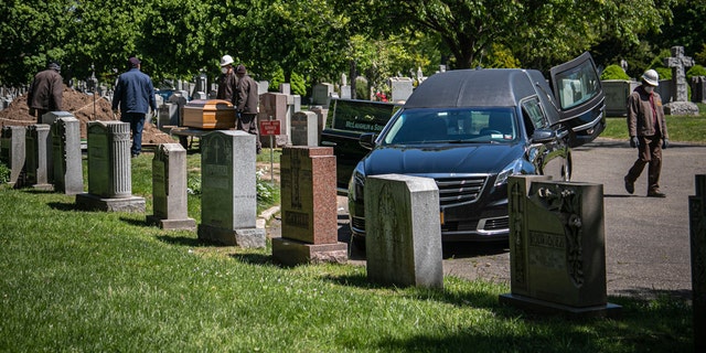 Cemetery workers prepare to bury a casket from McLaughlin & Sons funeral home, without any family present because of coronavirus restrictions, May 13, at Holy Cross Cemetery in the Brooklyn borough of New York. To help prevent the spread of the coronavirus, the casket is lowered and covered before relatives are allowed to the gravesite, following guidelines from the National Funeral Directors Association, according to a spokesman for the funeral home. (AP Photo/Bebeto Matthews)