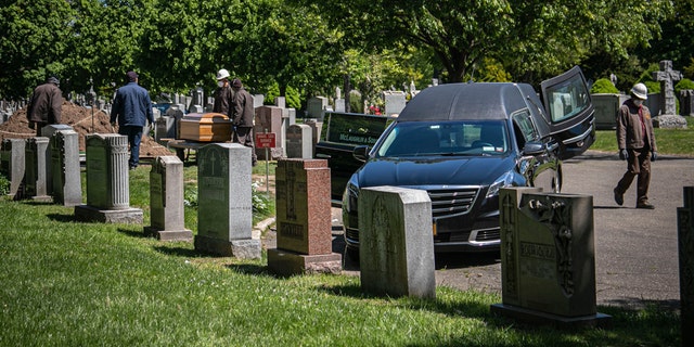 Cemetery workers prepare to bury a casket from McLaughlin & Sons funeral home, without any family present because of coronavirus restrictions, May 13, at Holy Cross Cemetery in the Brooklyn borough of New York. To help prevent the spread of the coronavirus, the casket is lowered and covered before relatives are allowed to the gravesite, following guidelines from the National Funeral Directors Association, according to a spokesman for the funeral home. (AP Photo/Bebeto Matthews)