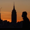 A man wearing a mask walks in front of the Empire State Building as the sun rises in New York City, May 14, 2020.