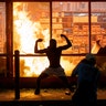 A man stands in front of a fire at an AutoZone store during a protest for George Floyd in Minneapolis, May 27, 2020. 