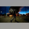 A man poses in the parking lot of an AutoZone store in flames, while protesters hold a rally against the death of George Floyd in Minneapolis on Wednesday, May 27, 2020. Violent protests over the death of the black man in police custody broke out in Minneapolis for a second straight night Wednesday, with protesters in a standoff with officers outside a police precinct and looting of nearby stores.