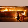 A protester carries a U.S. flag upside, a sign of distress, next to a burning building Thursday, May 28, 2020, in Minneapolis. Protests over the death of George Floyd, a black man who died in police custody Monday, broke out in Minneapolis for a third straight night.