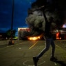 A man poses for a photo in the parking lot of an AutoZone store in flames, while protesters hold a rally for George Floyd in Minneapolis on Wednesday, May 27, 2020. Violent protests over the death of the black man in police custody broke out in Minneapolis for a second straight night Wednesday, with protesters in a standoff with officers outside a police precinct and looting of nearby stores.