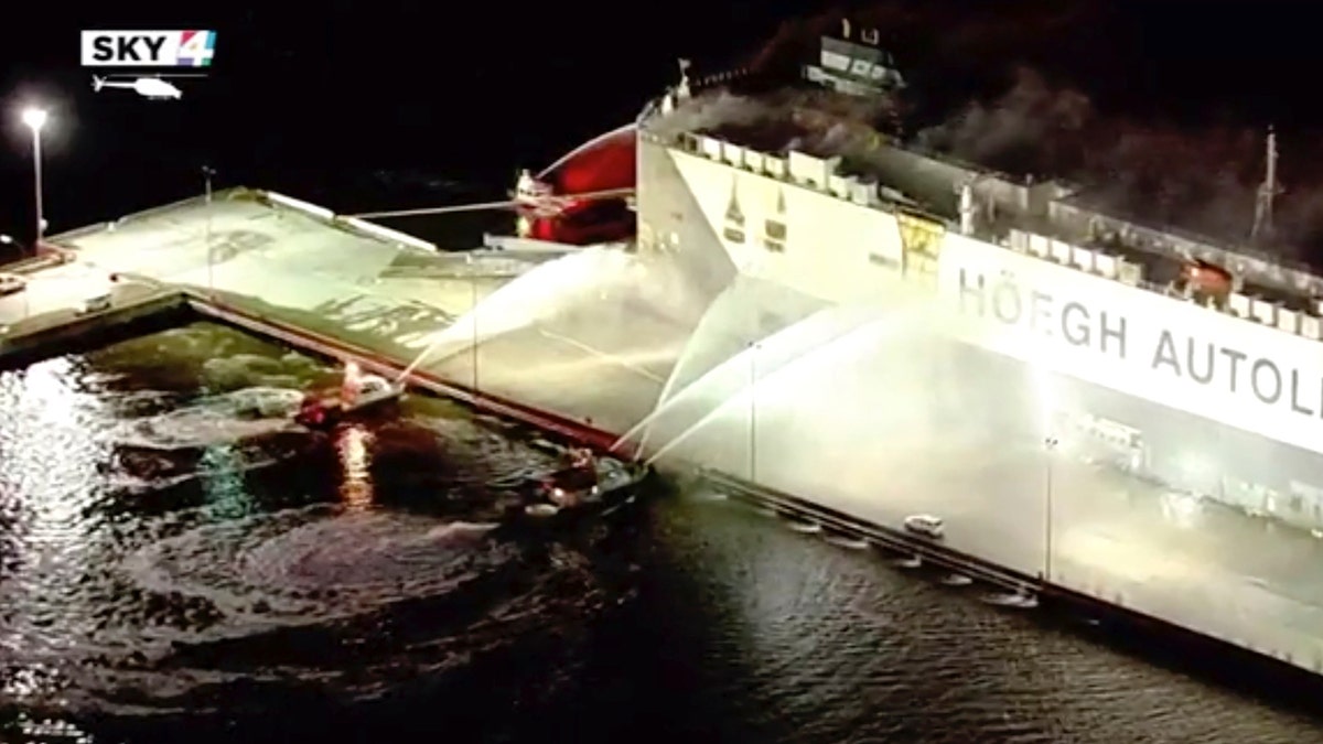 In this image made from aerial video taken on June 4, 2020, firefighters spray a cargo ship with water, in Jacksonville, Florida. Authorities say nine firefighters responding to a fire aboard a ship in Florida have been hospitalized after the ship exploded. The ship, a Norwegian vessel called Hoegh Xiamen was carrying old and used cars and had been scheduled to leave Jacksonville, First Coast News reported. (WJXT via AP)