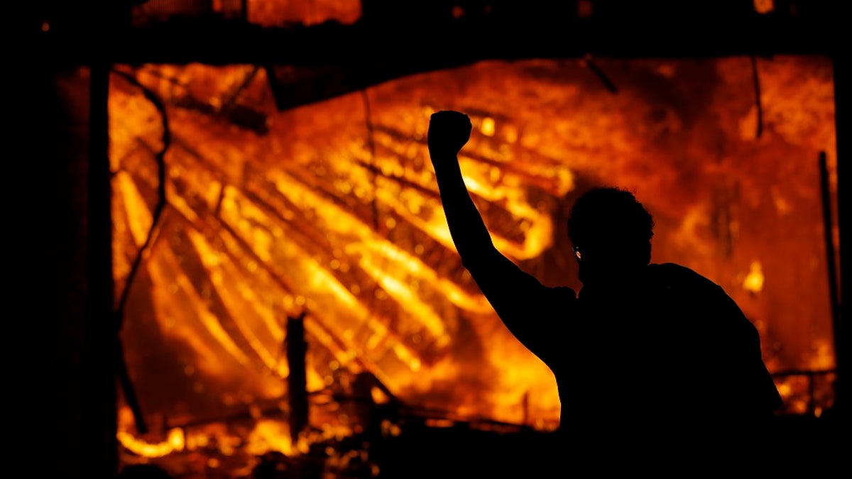 A protester gestures in front of the burning 3rd Precinct building of the Minneapolis Police Department on May 28, in Minneapolis. A suspect has been charged in connection with the suspected arson. (AP Photo/Julio Cortez)