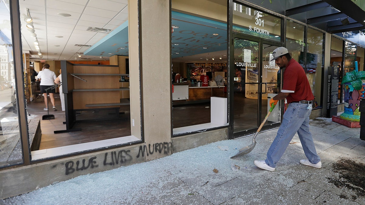 A worker sweeps broken glass from a window at the Louisville Visitors Center, early Saturday, May 30, 2020, in Louisville, Ky. The window was broken Friday evening during a protest over the deaths of George Floyd and Breonna Taylor. (AP Photo/Darron Cummings)