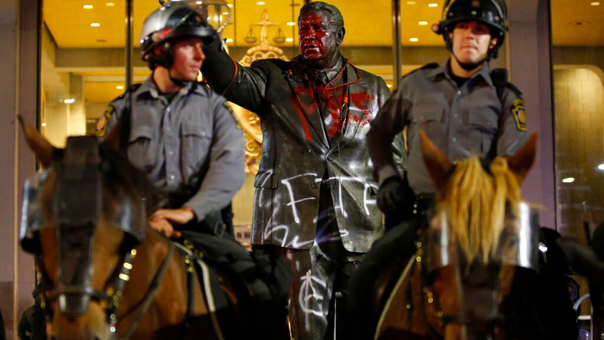 A vandalized statue of the late Philadelphia Mayor Frank Rizzo, who also served as the city's police commissioner, stands behind mounted State Police officers outside the Municipal Services Building in Philadelphia, The statue was vandalized during a protest over the death of George Floyd, a black man who died in Minneapolis police custody on May 25.