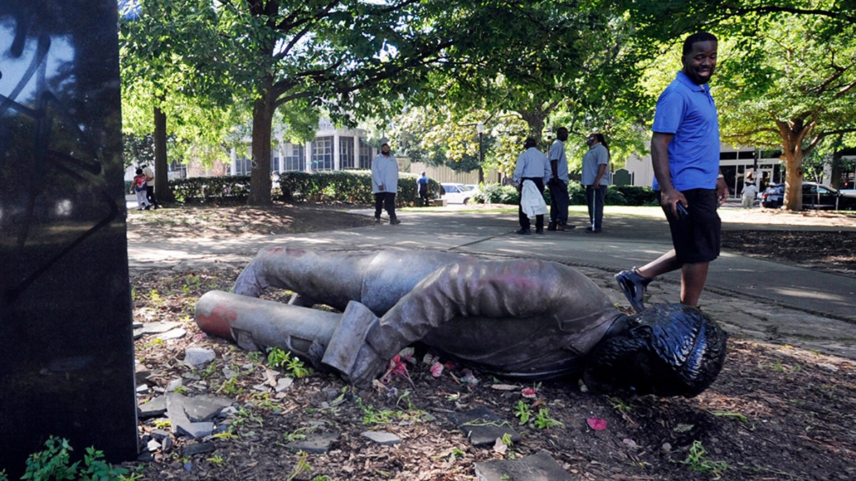An unidentified man walks past a toppled statue in Birmingham, Ala., on Monday, June 1, 2020, following a night of unrest. People shattered windows, set fires and damaged monuments in a downtown park after a protest against the death of George Floyd. Floyd died after being restrained by Minneapolis police officers on May 25. (AP Photo/Jay Reeves)