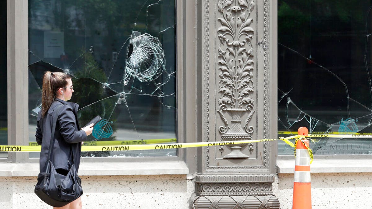 A woman walks past broken windows, Tuesday, June 2, 2020, in downtown Cleveland. The City of Cleveland extended its curfew through Tuesday night after riots broke out on Saturday over the death of George Floyd. (AP Photo/Tony Dejak)