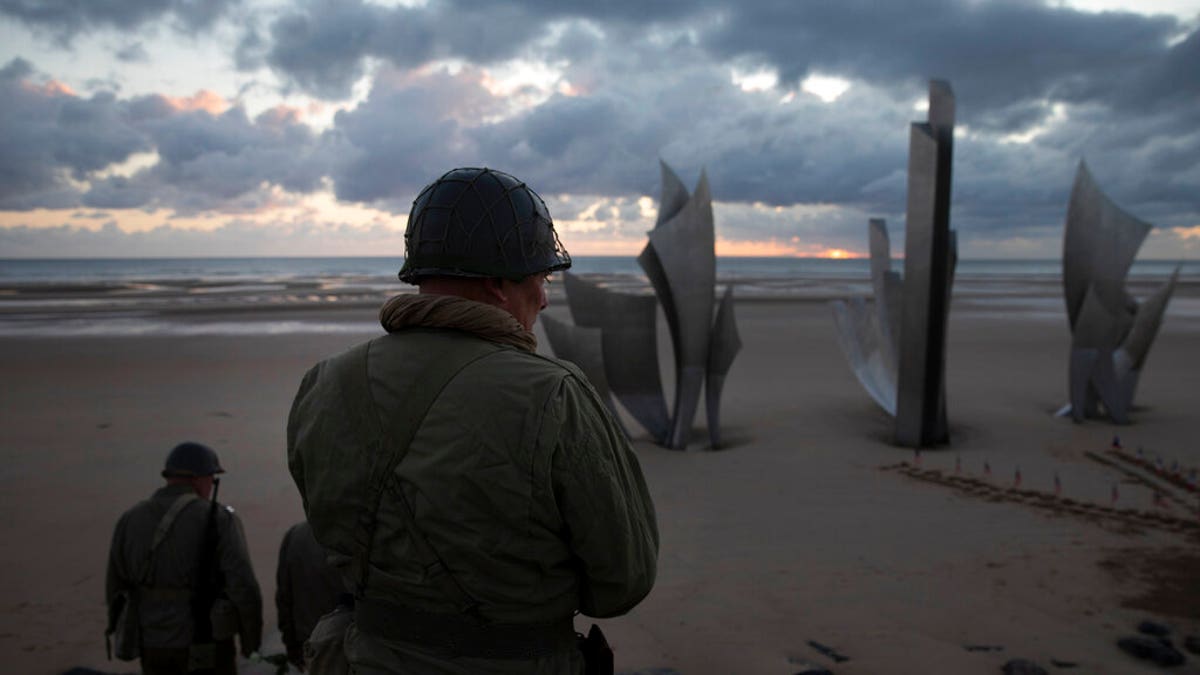 Two men in vintage US WWII uniforms walk toward the Les Braves monument at sunrise prior to a D-Day 76th anniversary ceremony in Saint Laurent sur Mer, Normandy, France, Saturday, June 6, 2020. Due to coronavirus measures many ceremonies and memorials have been cancelled in the region with the exception of very small gatherings.