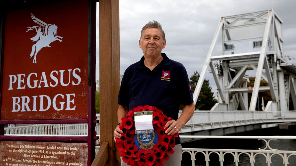 In this photo taken on Friday, June 5, 2020, British expatriate Steven Oldrid holds a poppy wreath as he stands on the site of the original WWII Pegasus Bridge in Benouville, Normandy, France. Due to coronavirus measures many relatives and veterans will not make this years 76th anniversary of D-Day. Oldrid will be bringing it to them virtually as he places wreaths and crosses for families and posts the moments on his facebook page. 