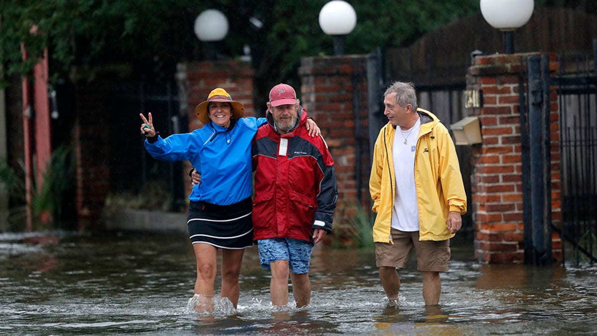 Isabelle Schneidau, left, gesturing to the camera as she walked in a rising storm surge with Mont Echols, center, and L.G. Sullivan, right, after checking on their boats in the West End section of New Orleans on Sunday.
