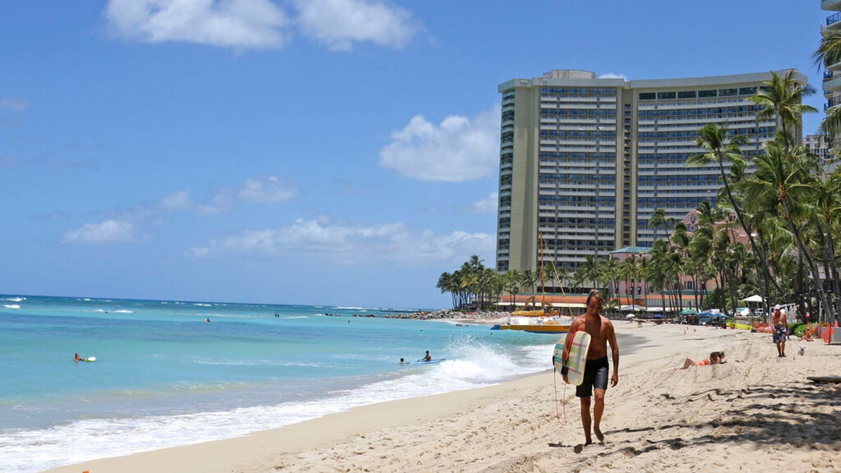 In this photo taken Friday, June 5, 2020, a surfer walks on a sparsely populated Waikiki beach in Honolulu.