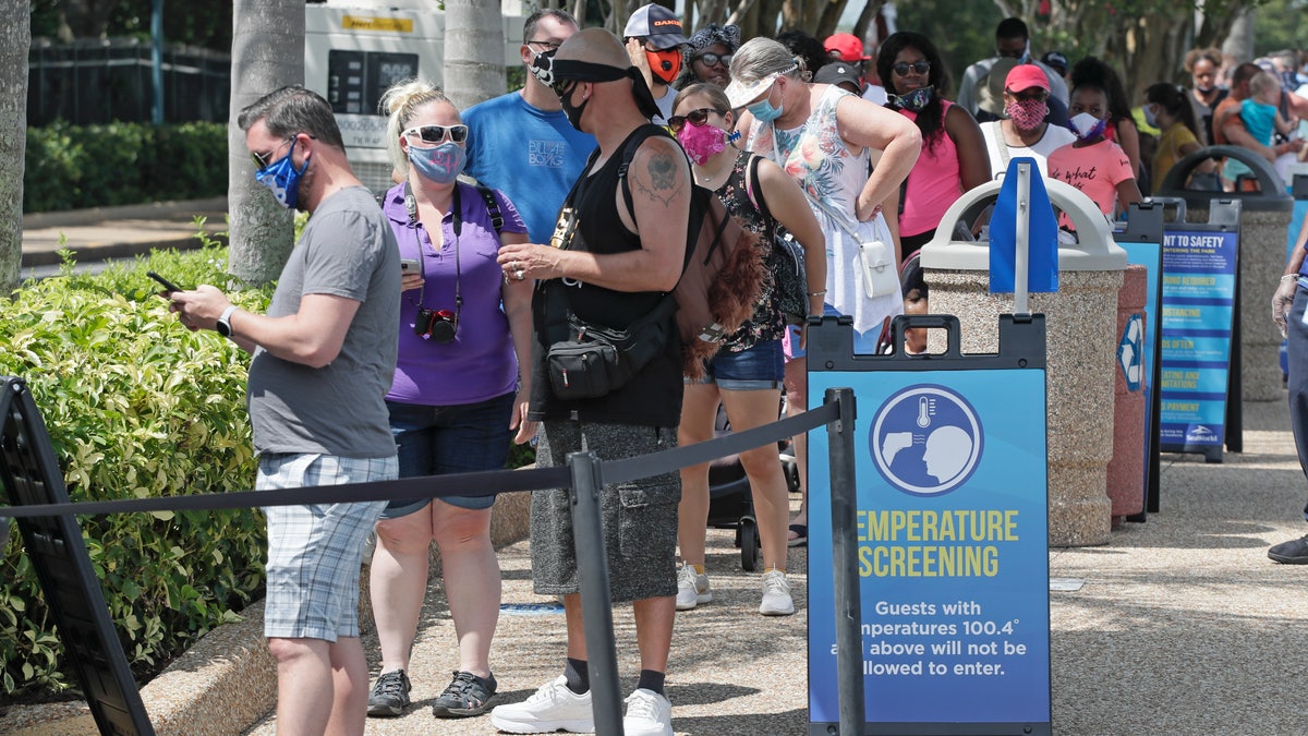 Guests wait in line to have their temperature taken before entering SeaWorld as it reopens with new safety measures in place, Thursday, June 11, 2020, in Orlando, Fla. The park had been closed since mid-March to stop the spread of the coronavirus. (AP Photo/John Raoux)