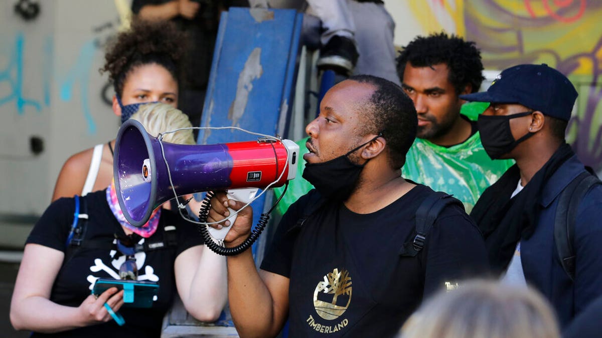 Mark Henry Jr., center, a Black Lives Matter leader, speaks into a megaphone in a doorway of the Seattle Police Department East Precinct building, which has been boarded up and abandoned except for a few officers inside, Thursday, June 11, 2020, in Seattle. 