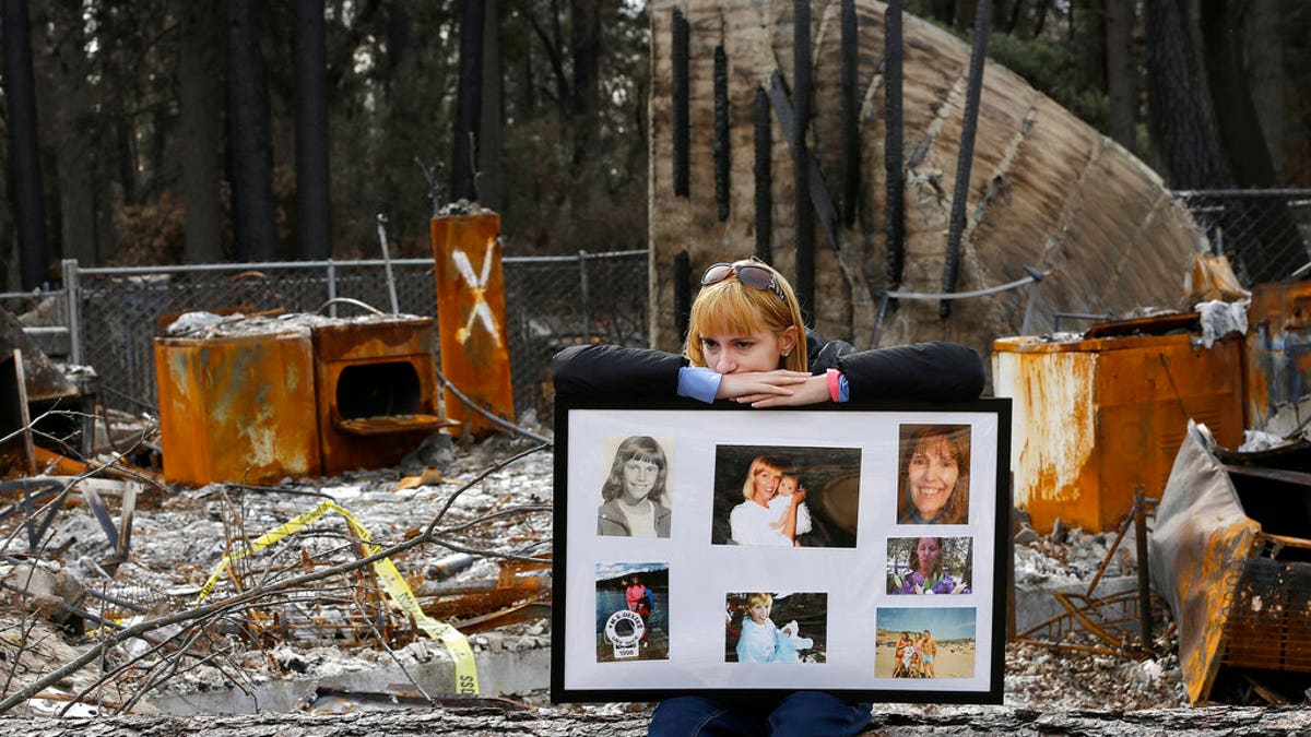 FILE: Christina Taft, the daughter of Camp Fire victim Victoria Taft, displays a collage of photos of her mother, at the burned-out ruins of the Paradise, Calif.
