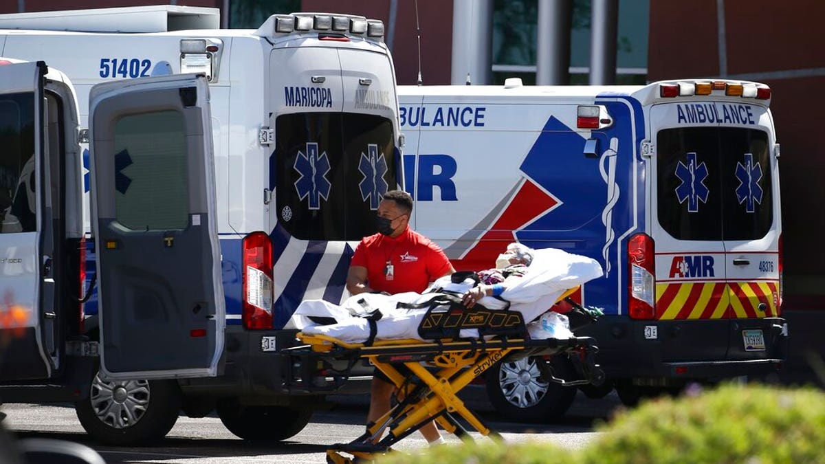 A person is brought to a medical transport vehicle from Banner Desert Medical Center as several transports and ambulances are shown parked outside the emergency room entrance, June 16, in Mesa, Ariz. 