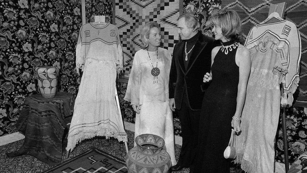 FILE - In this Nov. 26, 1974 file photo, Marlon Brando, center, Ethel Kennedy, left, and Jean Kennedy Smith stand amid Native American Indian artifacts at the American Indian Development Dinner at the Waldorf-Astoria Hotel in New York. Jean Kennedy Smith, the youngest sister and last surviving sibling of President John F. Kennedy, died at 92, her daughter confirmed to The New York Times, Wednesday, June 17, 2020. (AP Photo/Richard Drew, File)