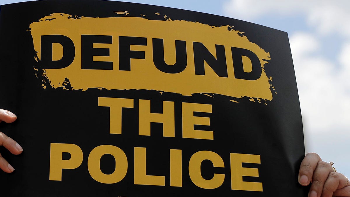A person holds up a defund the police sign