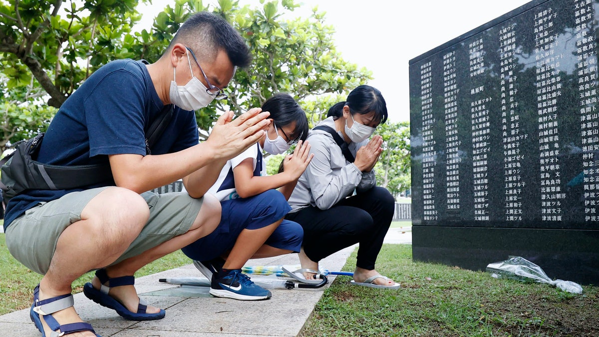 Members of a bereaved family pray in front of a "Cornerstone of Peace" monument wall on which the names of all those who lost their lives, both civilians and military of all nationalities in the Battle of Okinawa are engraved, at the Peace Memorial Park in Itoman, Okinawa, Japan, Tuesday, June 23, 2020. (Kyodo News via AP)