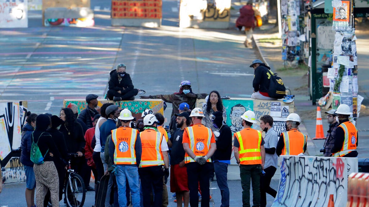 Seattle Department of Transportation workers talk with protest organizers near the Seattle Police Department East Precinct building after SDOT arrived at the CHOP (Capitol Hill Occupied Protest) zone in Seattle, Friday, June 26, 2020, with the intention of removing barricades that had been set up in the area. (AP Photo/Ted S. Warren)