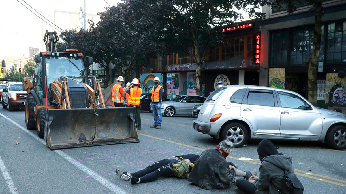 Protesters lie down and sit in the street after workers and heavy equipment from the Seattle Department of Transportation arrived at the CHOP (Capitol Hill Occupied Protest) zone in Seattle, Friday, June 26, 2020, with the intention of removing barricades that had been set up in the area. (AP Photo/Ted S. Warren)