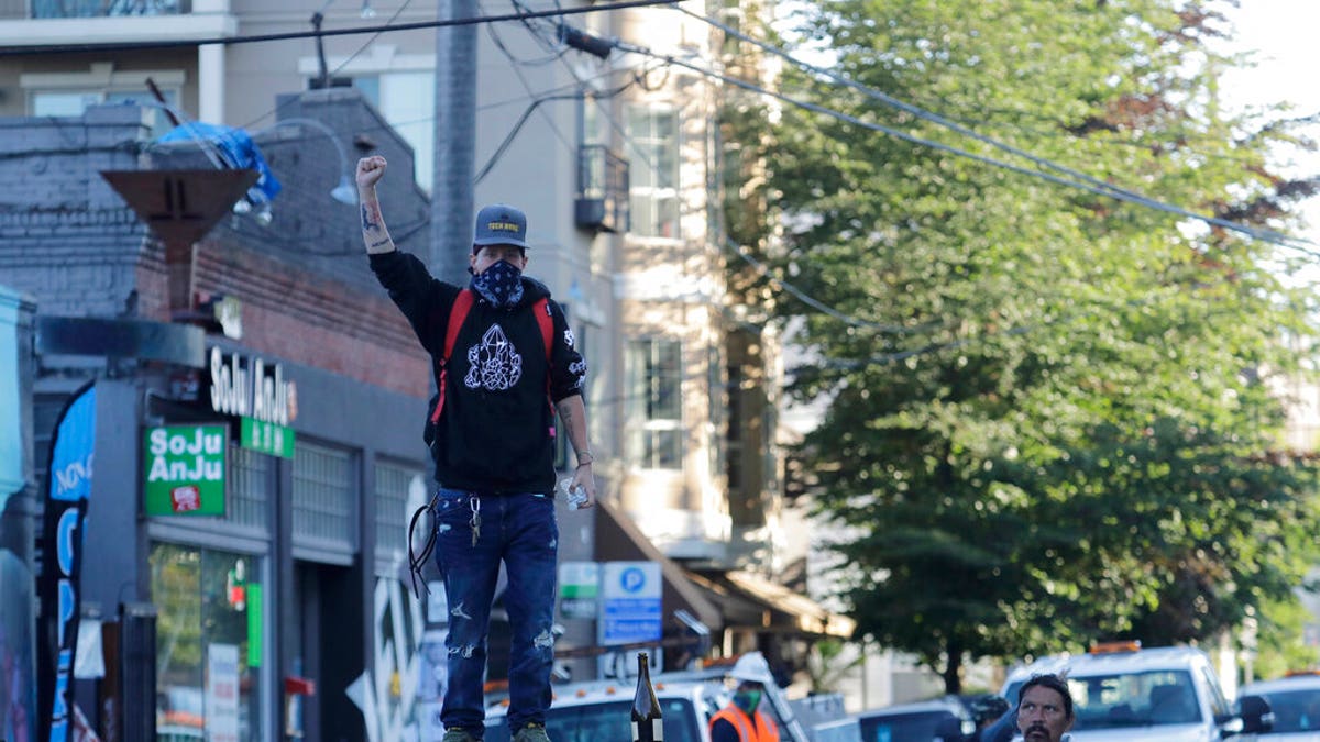 A protester stands on a barricade with his fist raised, Friday, June 26, 2020 at the the CHOP (Capitol Hill Occupied Protest) zone in Seattle after workers and trucks from the Seattle Department of Transportation arrived with the intention of removing barricades that had been set up in the area, which has been occupied by protesters since Seattle Police pulled back from their East Precinct building following violent clashes with demonstrators earlier in the month, but left after meeting resistance from protesters. 