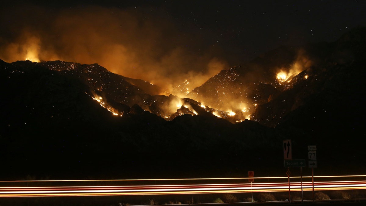 Vehicle lights leave streaks a the Bighorn Fire moves along the western side of the Santa Catalina Mountains, Sunday, June 14, 2020, in Oro Valley, Ariz.
