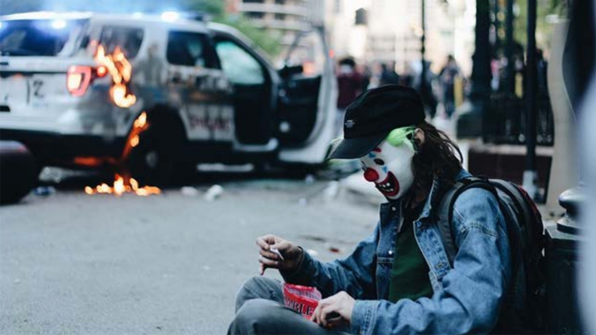In the images, the masked man can be seen handling a police vehicle’s gas tank and later sitting and posing near the flaming SUV. (Courtesy: DOJ)