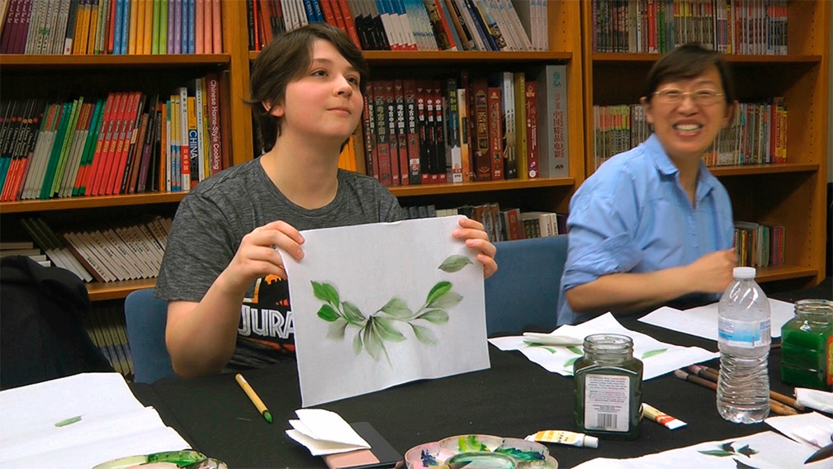 Undergraduate student Moe Lewis, left, shows her watercolor painting of peony leaves at a traditional Chinese painting class at the Confucius Institute at George Mason University in Fairfax, Va., on May 2, 2018. (AP Photo/Matthew Pennington)