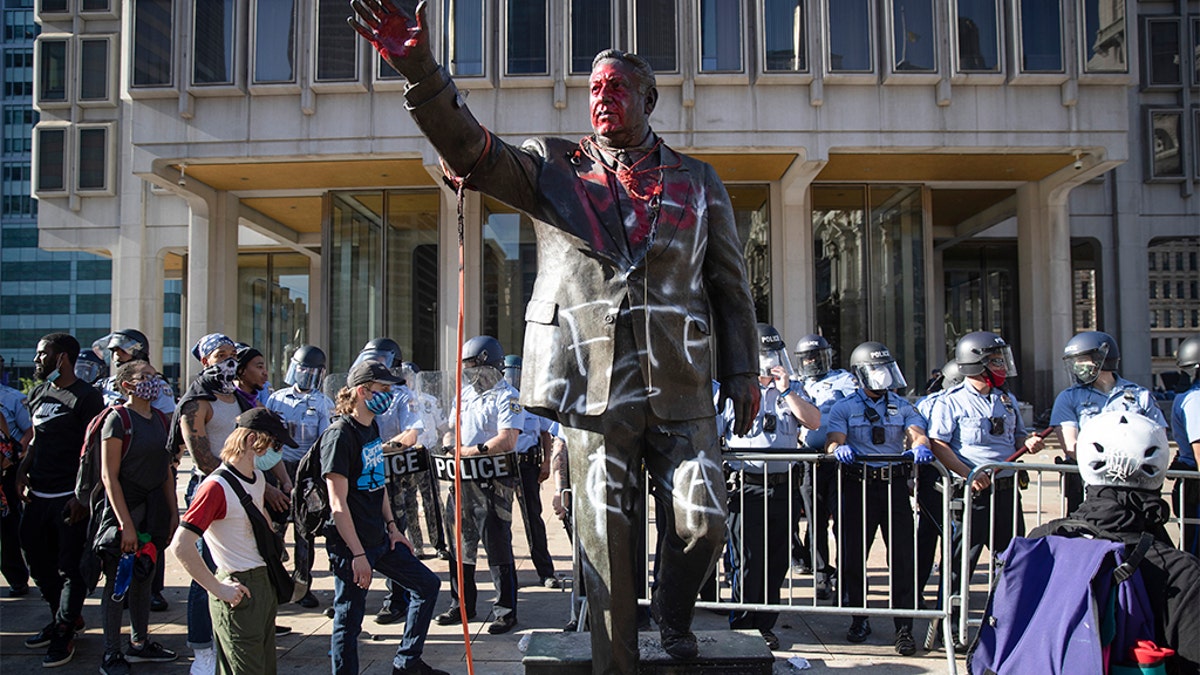 In this Saturday, May 30, 2020 photo police stand near a vandalized statue of controversial former Philadelphia Mayor Frank Rizzo in Philadelphia, during protests over the death of George Floyd, who died May 25 after he was restrained by Minneapolis police. Workers early Wednesday, June 3 removed the statue which was recently defaced during the weekend protest.