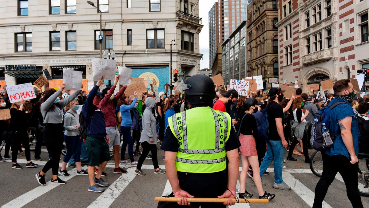 A police officer holding a baton stands by as people march to call for Police Department reform as part of the "Unite Against Racist Police Terror! Boston Speakout and March" in Boston, Massachusetts on June 7, 2020. - Protesters have rallied for racial justice in cities across the United States following the death of George Floyd at the hands of police on May 25. (Photo by Joseph Prezioso / AFP) (Photo by JOSEPH PREZIOSO/AFP via Getty Images)