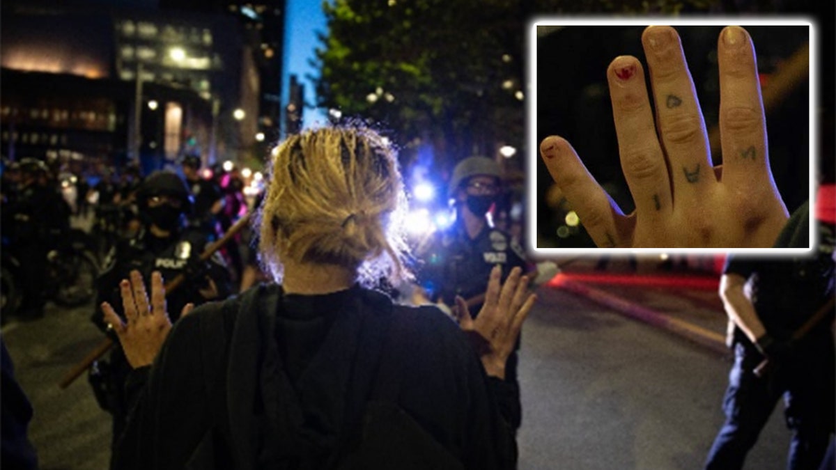 A separate image shows a woman raising her hands across from police – and in it tattoos on her knuckles are visible. 