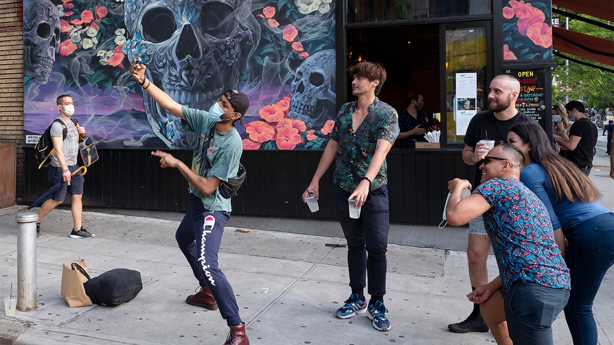 A man takes photos with friends outside a bar in the Hell's Kitchen neighborhood of New York, Friday, May 29, 2020, during the coronavirus pandemic. People are beginning to gather in small groups as the city begins to reopen. (AP Photo/Mark Lennihan)