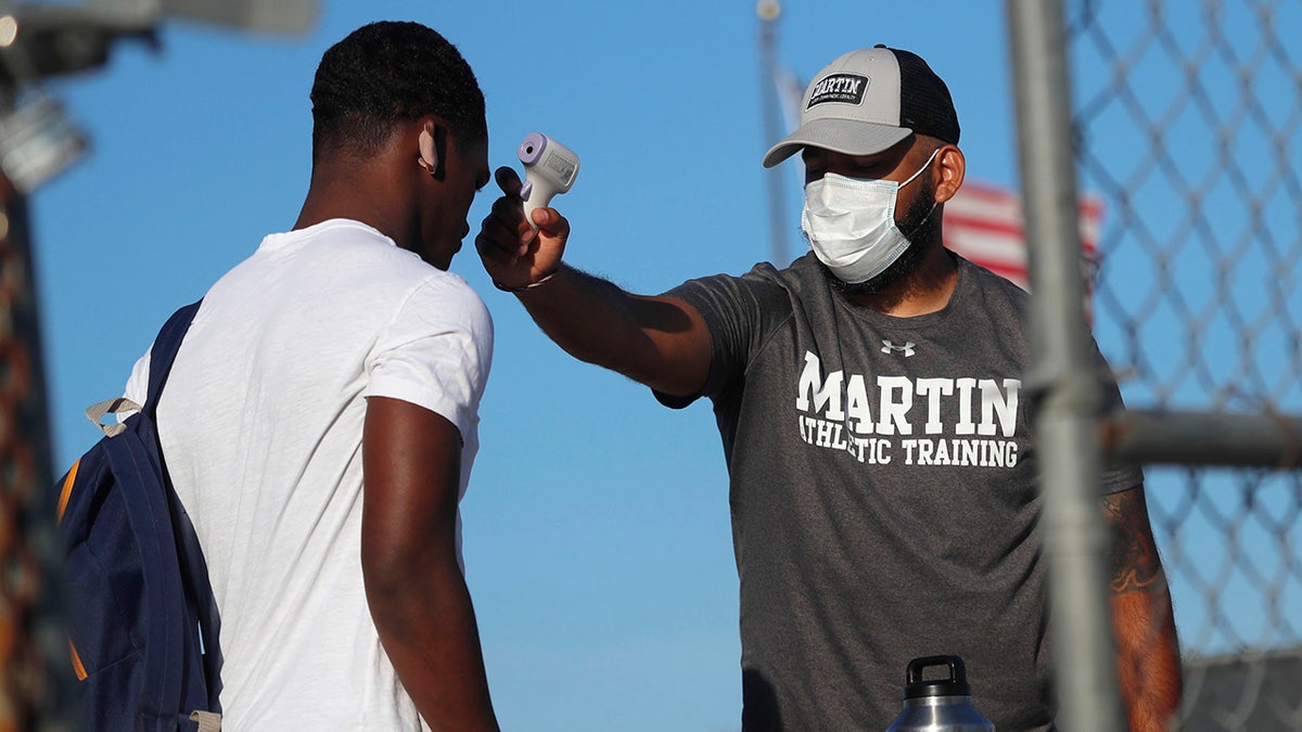 Before entering the field gates for football strength and conditioning camp at Arlington Martin High School, athletic Trainer Joey Pena, right, uses a thermometer to check the temperature of sophomore running back Gervawn Neville on Thursday, June 18, 2020, in Arlington, Texas. (AP Photo/LM Otero)