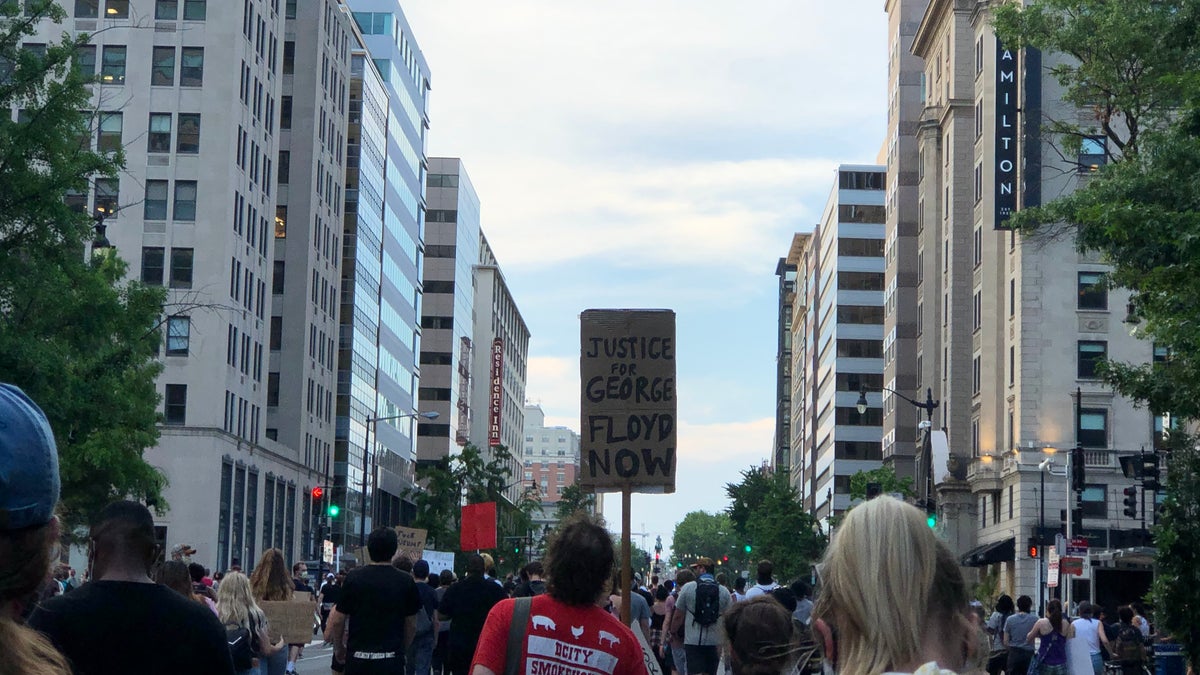 Demonstrators carry signs reading, for example, "Justice for George Floyd Now."