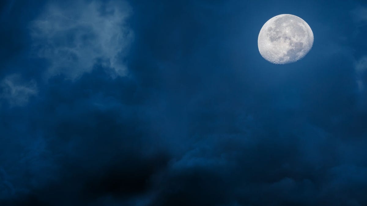 Moon at night with bright and dark clouds on blue background