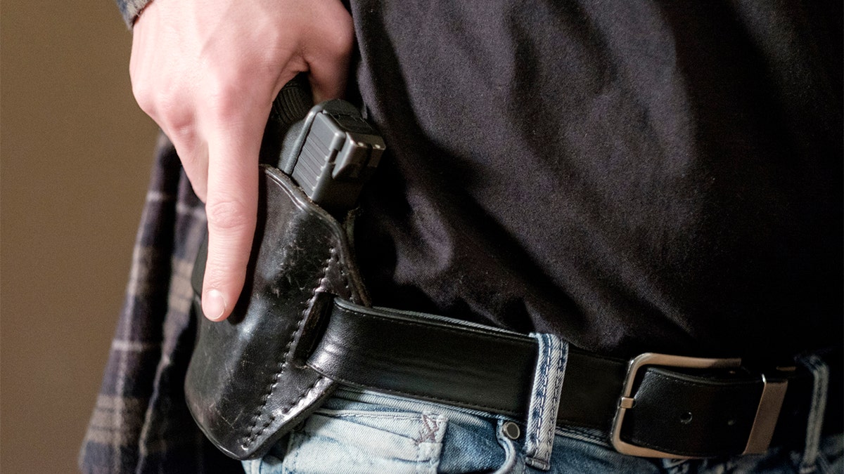 A man carries a gun in a leather holster on his belt.